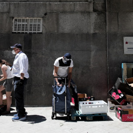 Dos personas recogen alimentos que les dan dos voluntarios a las puertas de la Parroquia Santa María Micaela donde han acudido para recibir una ayuda alimentaria. Eduardo Parra / Europa Press / Archivo