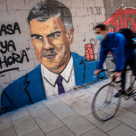 VALENCIA, 26/10/2020.Una persona en bicicleta pasa frente a una pintura mural del artista urbano J.Warx donde aparece el presidente del Gobierno, Pedro Sánchez, bajo la frase “A casa que ya es hora".