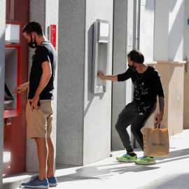 Dos jóvenes operan en sendos cajeros automáticos de dos entidades bancarias, en la localidad malagueña de Ronda. REUTERS/Jon Nazca