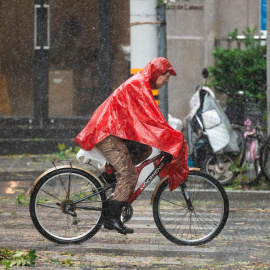 Un hombre pedalea en bicicleta entre la lluvia y el viento provocadas por el tifón Bebinca este lunes en Shanghai (China).