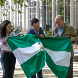 El presidente de la Junta de Andalucía, Juanma Moreno (c) entrega una bandera andaluza al creador del Reto Pelayo Vida, Eric Frattini (d) y a la expedicionaria almeriense Felisa Requena (i) antes de despedir a la expedición de la nueva edición.