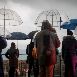 Varias personas se protegen de la lluvia con sus paraguas este miércoles en la terraza del centro cultural Tabakalera de San Sebastián