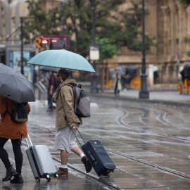 Una pareja con maletas se protegen de la lluvia bajo sus paraguas en Sevilla-21/10/2022