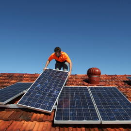 Un operario trabaja colocando paneles solares en un tejado de una vivienda.