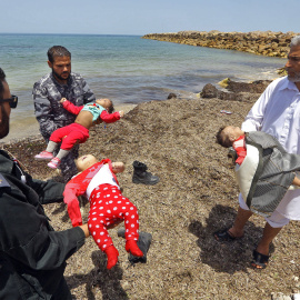 Guardacostas libios sostienes los cadáveres de tres bebés fallecidos en el naufragio frente a las costas libias. Hay cien desaparecidos y 16 supervivientes.- AFP/ MAHMUD TURKIA