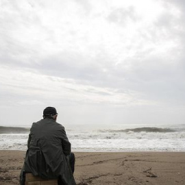 Un hombre mira al  mar en una playa mientras está nublado.