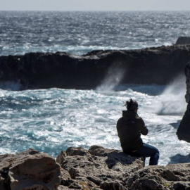 Un joven observa romper las olas en un fuerte oleaje en Menorca.