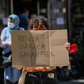 Una dona, acompanyada per membres de la Xarxa veïnal de Suport Mutu Ciutat Vella, agafa una pancarta en la qual es pot llegir "Renda bàsica garantida". 22 de maig del 2020.