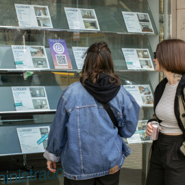 Dos personas observan la oferta de pisos en alquiler de una oficina inmobiliaria de Barcelona, a 12 de marzo de 2024.