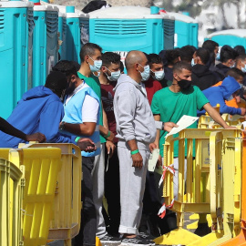 Varios migrantes esperan en el muelle de Arguineguín (Gran Canaria) a que les tomen las huellas dactilares y la filiación.