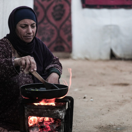 Mujer palestina desplazada cocina fuera de su tienda de campaña.