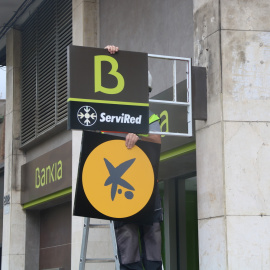 Un operari canviant el logotip de Bankia pel de CaixaBank a l'oficina situada al número 116 de la Rambla del Poblenou de Barcelona. Imatge de 6 d'abril de 2021.