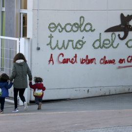 Una mare acompanya els seus fills a l'escola Turó del Drac de Canet de Mar. Una pintada reclama l'ensenyament en català a la façana del centre.