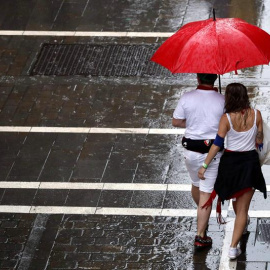 Dos personas se protegen de la lluvia en una de las céntricas calles de Pamplona durante la fiesta de San Fermín. Navarra está en alerta amarilla este lunes por lluvias y tormentas, según Aemet. EFE/ Javier Lizón