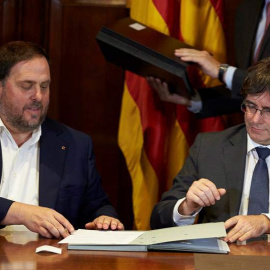 El presidente de la Generalitat, Carles Puigdemont (derecha), acompañado por el vicepresidente Oriol Junqueras, firma la convocatoria de referéndum. | ALEJANDRO GARCÍA (EFE)