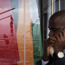 Un hombre habla por su teléfono móvil mientras pasa por una ventana en la que se reflejan las banderas de los BRICS, a 2 de junio de 2023 en Cape Town