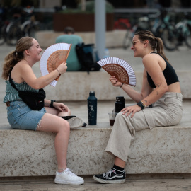 31/07/2023.- Dos jóvenes combaten el calor con sendos abanicos en este último día de julio en el País Valencià.