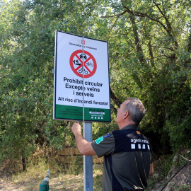 Un Agent Rural obre un cartell de prohibició del pas al Montsec a la zona de Corçà, a Àger, per l'activació del pla Alfa 3