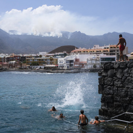 Varias personas disfrutan este lunes de un día de playa en el Puertito de Güímar, desde donde se puede ver el incendio que afecta a la isla de Tenerife desde hace seis días.