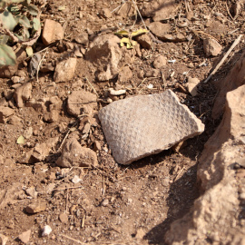 Un tros d'amiant enmig de la sorra i les pedres a la zona de les bateries del Turó de la Rovira