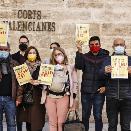 Imagen de archivo en la que varias personas sostienen el 'Informe de Denuncias de los derechos lingüísticos en el País Valencià, frente a las puertas de Les Corts, en diciembre de 2021.