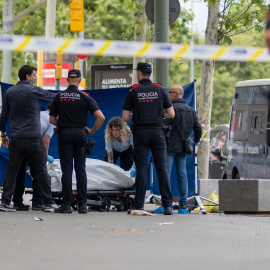 Agentes de los Mossos d'Esquadra y trabajadores de la funeraria levantan el cadáver del joven fallecido, en el paseo Joan de Borbó, en Catalunya.