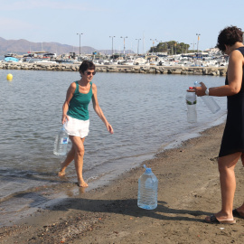 Dues dones omplen ampolles i garrafes del mar a la platja del Port de la Selva