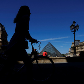 11/05/2022-Una mujer camina con su bicicleta cerca de la Pirámide de cristal del museo del Louvre París, Francia, el 11 de mayo