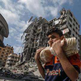 16/10/23 Un joven palestino porta dos bolsas de pan este lunes 16 de octubre frente a un edificio bombardeado en el barrio de Al Remal, en la ciudad de Gaza.