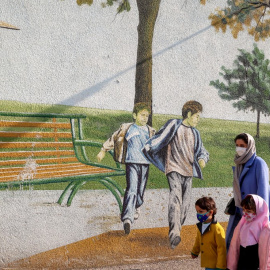 Una mujer pasea junto a sus hijos frente a un mural infantil en Teherán.