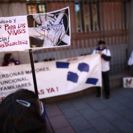 Una mujer con un cártel en el que se lee: `Por dignidad y derechos para los vivos, Justicia para los fallecidos´ durante una concentración de familiares de usuarios de residencias frente a la Consejería de Políticas Sociales "por una gestión públic