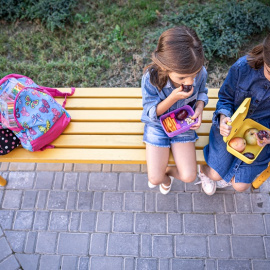 Niñas de la escuela sentadas en un banco en el patio de la escuela y comiendo de las loncheras