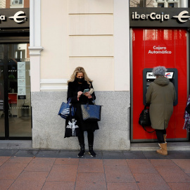 Una mujer utiliza el cajero automático de una oficina de Ibercaja en Madrid, mientras otras esperan. REUTERS/Juan Medina