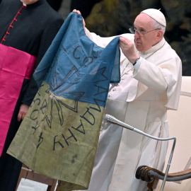 12/04/2022 - El papa Francisco muestra una bandera de Ucrania que fue enviada desde la localidad de Bucha durante la audiencia semanal en el Salón de Pablo VI en el Vaticano.