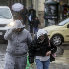 Foto de archivo de dos personas tapándose la cabeza con la capucha de la chaqueta como consecuencia de la lluvia