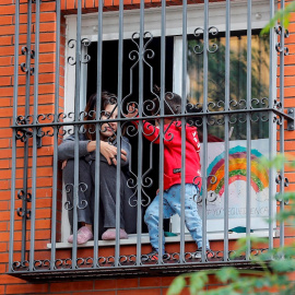 Una joven y un niño asomados entre las rejas de una ventana de una vivienda. EFE/José Manuel Vidal/Archivo