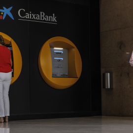 31/05/2024 Dos personas en los cajeros dispuestos en el edificio de la sede de Caixabank, en Valencia. Foto de archivo.