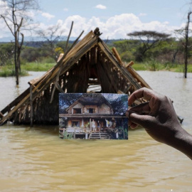 Un hombre sujeta una fotografía que muestra cómo era su hogar en Kenia antes de una inundación.