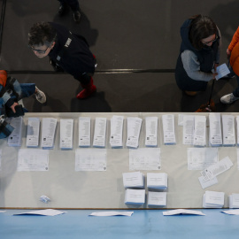 Varias personas escogen papeletas para ejercer su derecho al voto en el pabellón polideportivo Ames en A Coruña durante la jornada electoral en Galicia, este domingo.