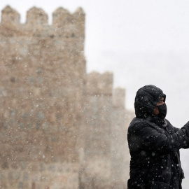 Un hombre se hace una foto con su teléfono móvil junto a la muralla de Ávila durante la primera nevada del otoño en la capital abulense.