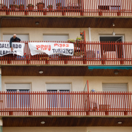 Un hombre coloca una pancarta en el balcón de su casa en protesta por los pisos turísticos del edificio en el que vive, en el barrio de Sants en Barcelona. La pancarta dice "No más pisos turísticos". REUTERS/Albert Gea