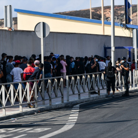 Agentes de Policía supervisan a cientos de personas, la mayoría marroquíes, que guardan cola en la oficina para tramitar los asilos situada en la frontera del Tarajal que separa Ceuta de Marruecos, a 3 de agosto de 2021, en Ceuta (España). Imagen de a