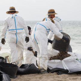 Varios operarios trabajan en la limpieza de la playa afectada por el vertido de hidrocarburos en València, a 17 de julio de 2024.