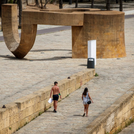 Dos personas pasean este sábado bajo un intenso Sol en el Muelle de la Sal, en Sevilla. - EFE