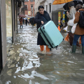 Una turista carga su maleta con ruedas para evitar que toque el "agua alta" en Venecia (Italia), este viernes. EFE/Andrea Merola