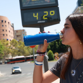 14/08/2024 Una joven bebe agua en la calle en Sevilla este agosto. Al fondo, un termómetro.