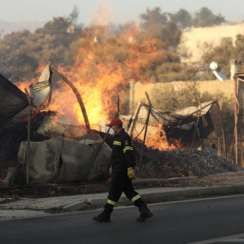 13/08/2024 Un bombero pasa junto al incendio forestal que arrasa un negocio de leña, en Penteli, al noreste de Atenas. Foto de archivo.