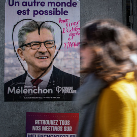 Una mujer camina en París el 9 de abril de 2022 frente a un cartel de campaña de La Francia Insumisa (LFI), partido liderado por Jean-Luc Mélenchon.