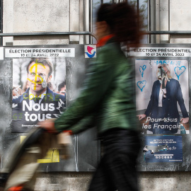 Una mujer camina junto a vallas publicitarias con carteles de los candidatos presidenciales franceses Macron y Le Pen, en París, Francia, el 18 de abril de 2022. Macron se enfrentará a la candidata del partido francés de extrema derecha Rassemblement N