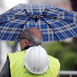 Un trabajador de la construcción se protege de la lluvia con un paraguas en Valencia. EFE/Kai Försterling